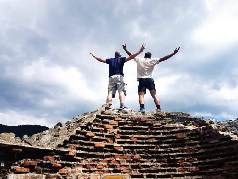 Two men seen from behind standing on a ruined brick structure